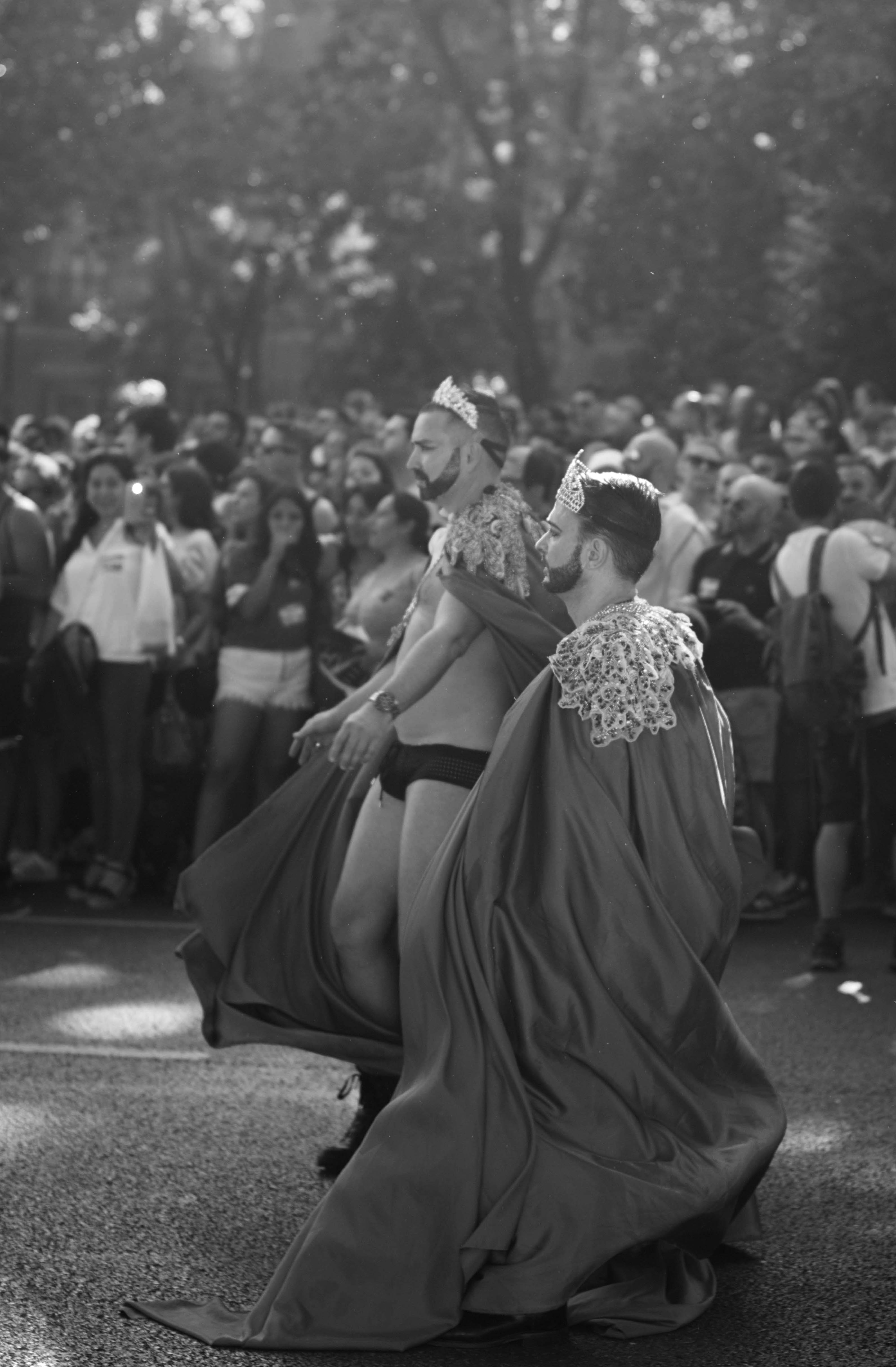 a black and white photo of two people in long flowing capes in a pride parade