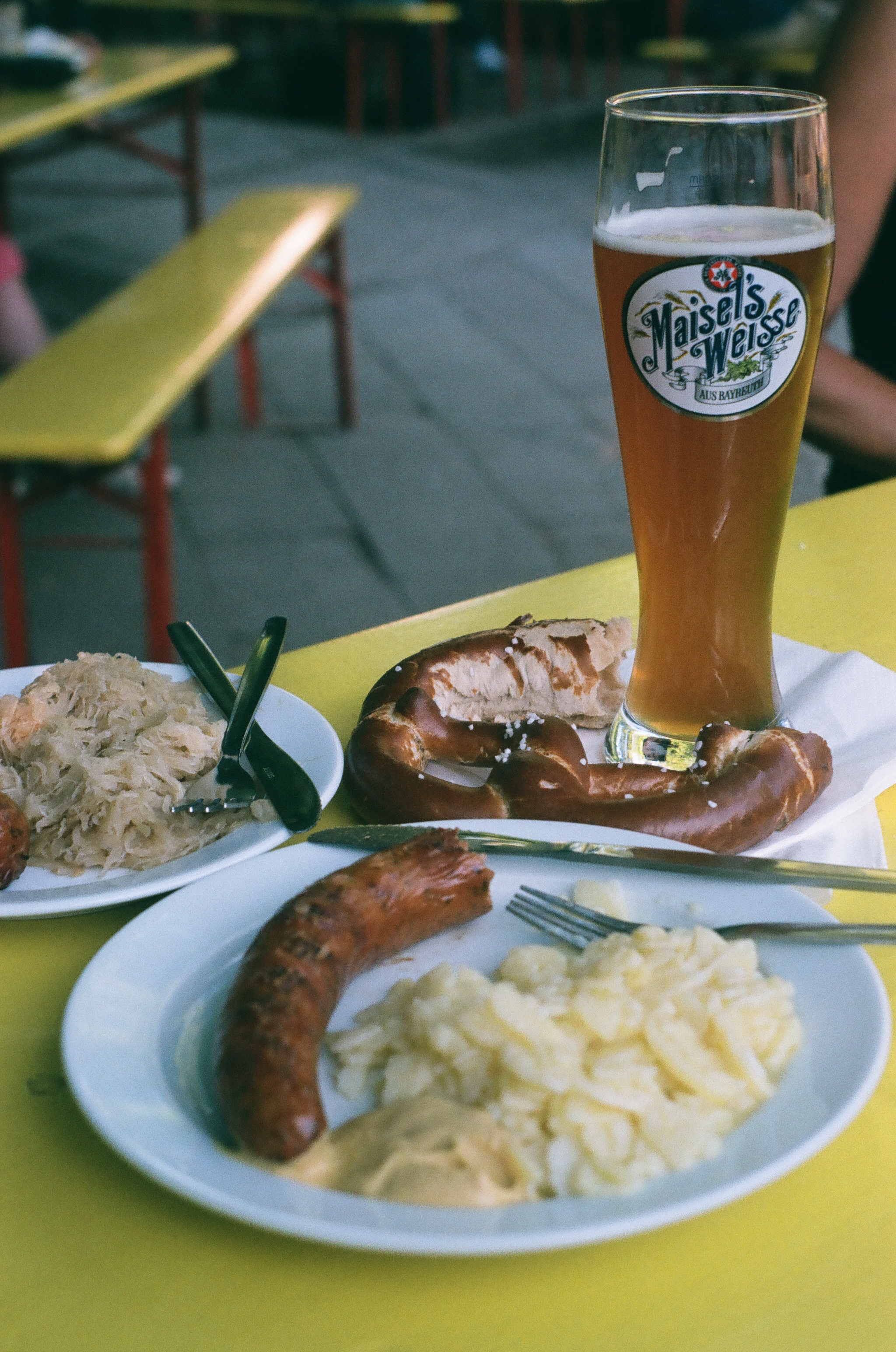 a german beer garden tabletop spread including a wheat beer, sausage, and pretzel