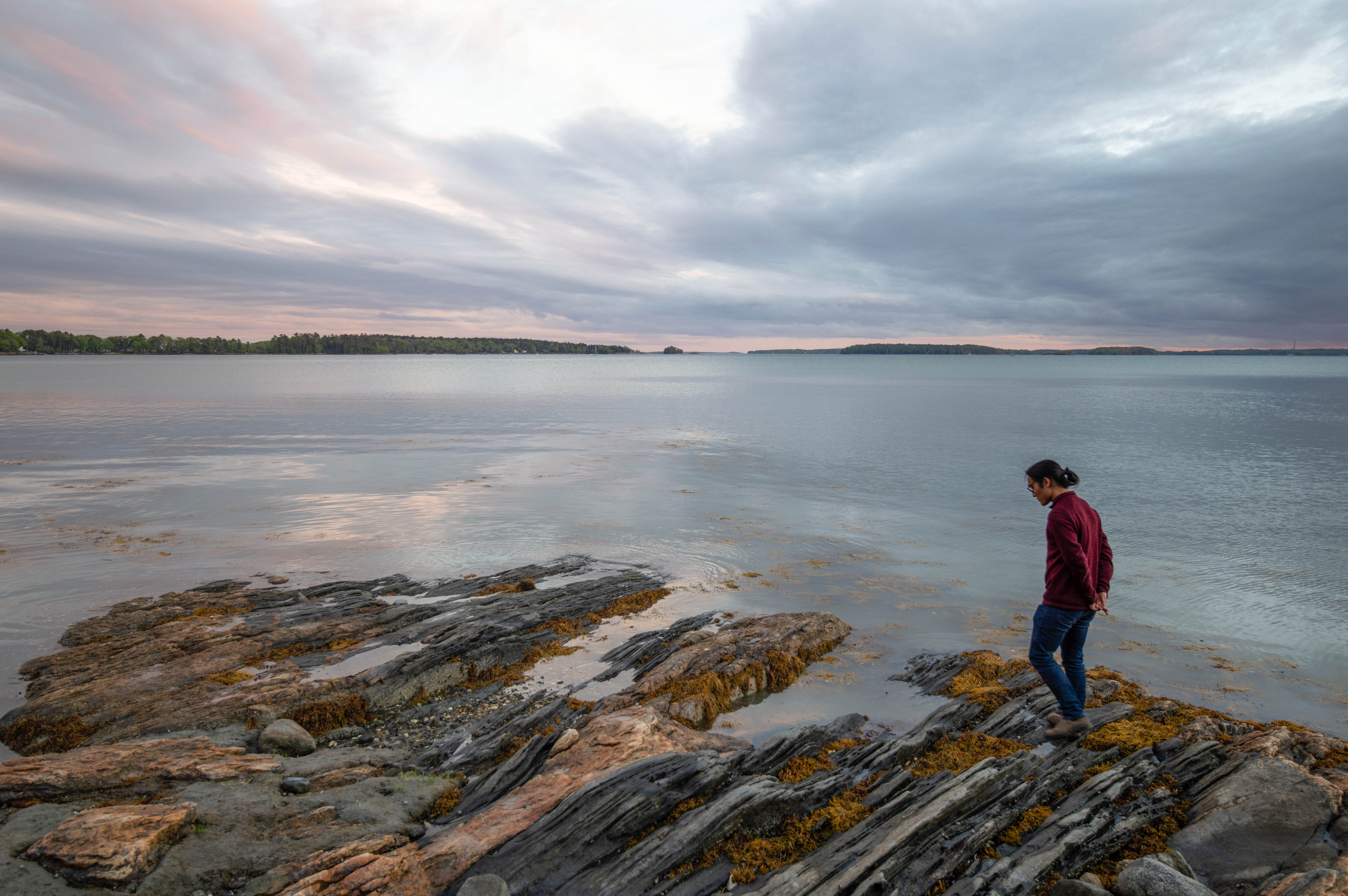 a man with long hair in a bun walks by a tidepool at sunset