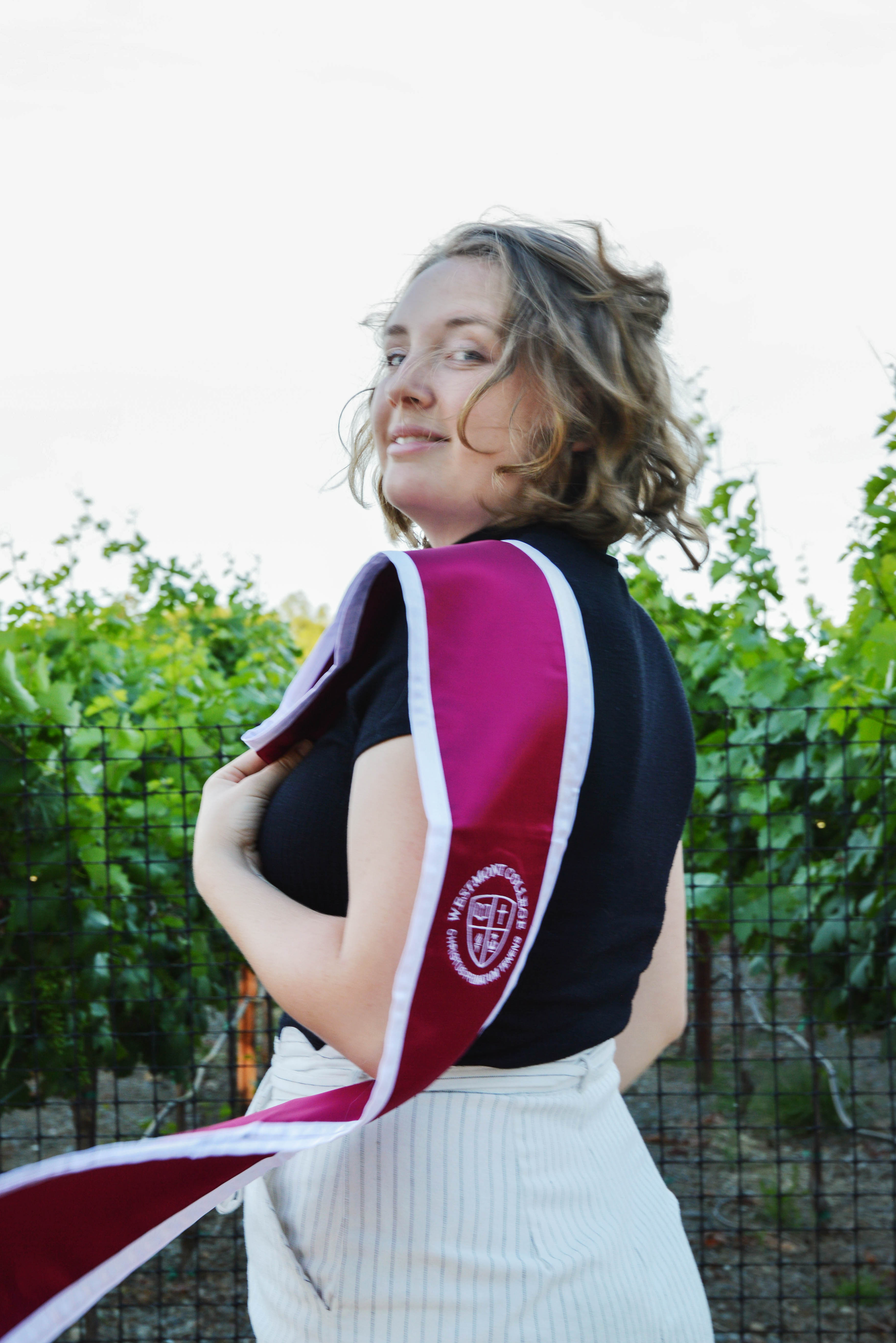 a young woman smiling over her shoulder wearing a graduation stole