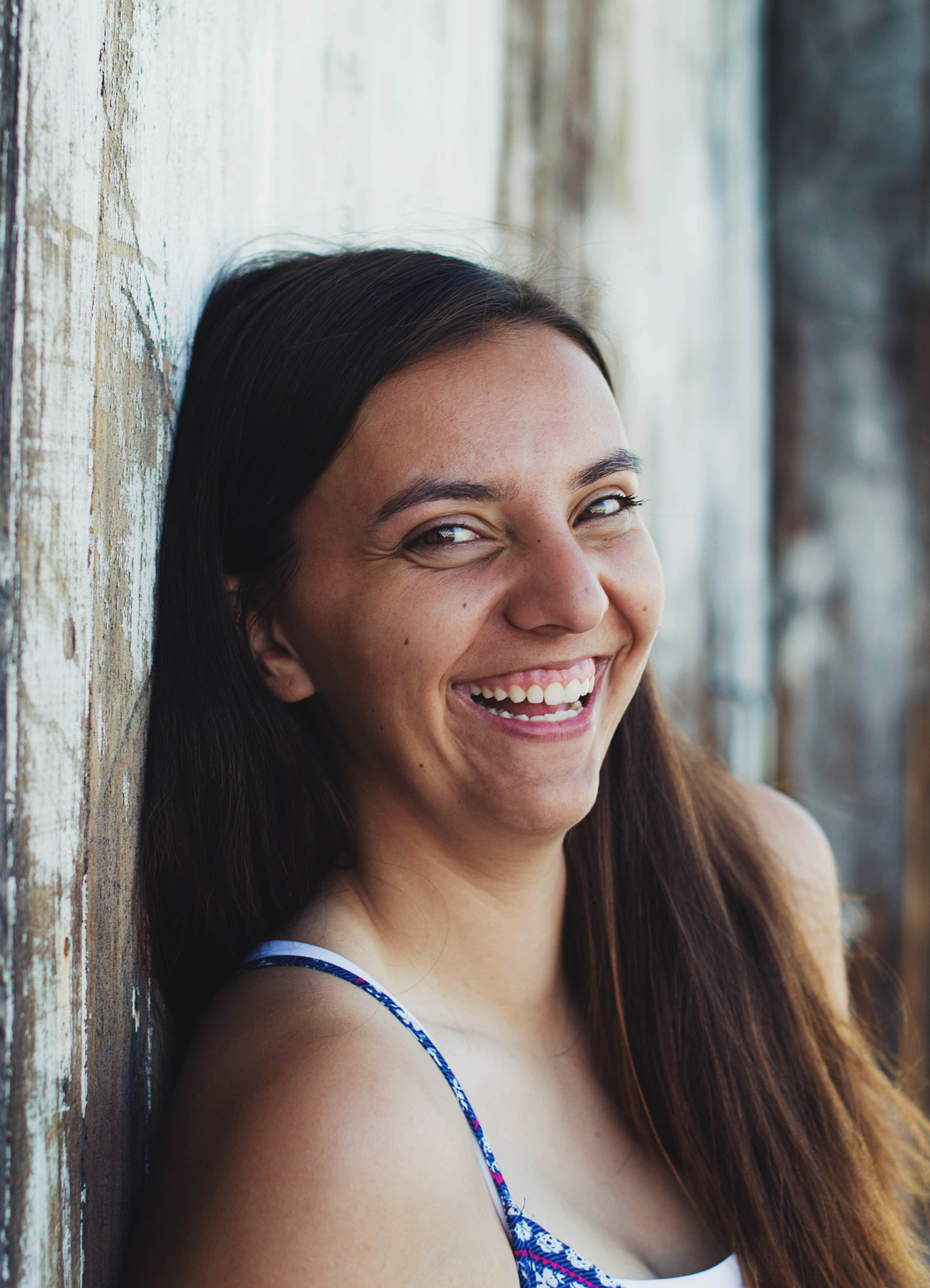 a young woman leans against a wooden wall laughing